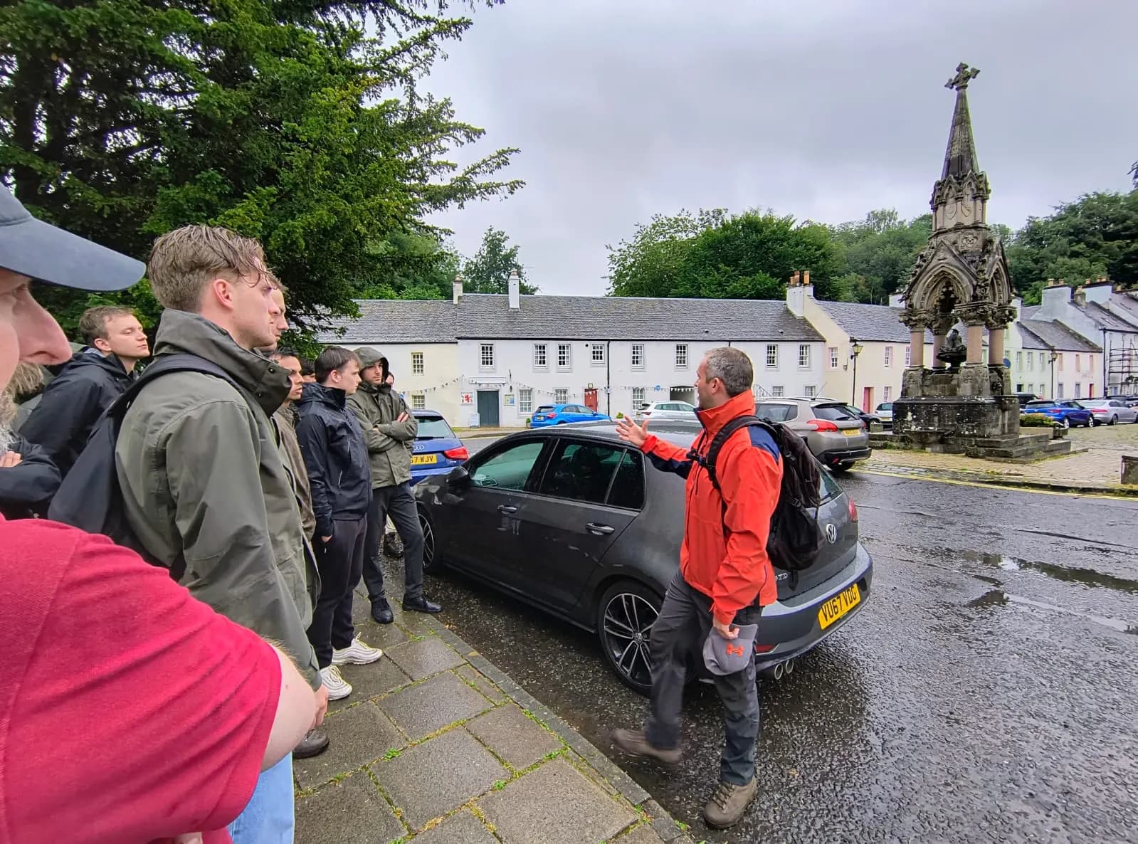 A tour group gathered beside a memorial in a Scottish village